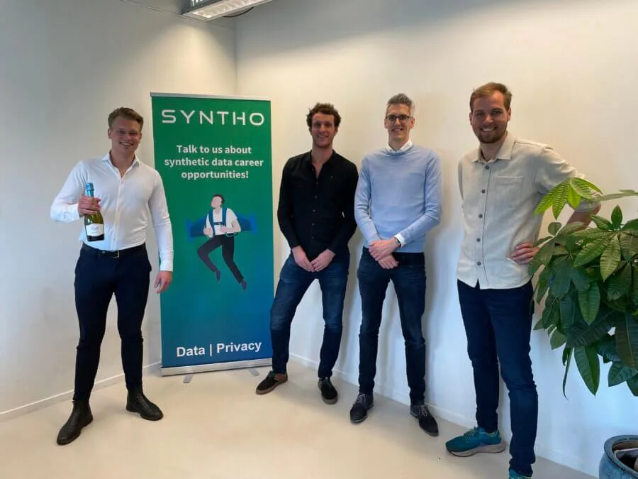 Teamleden van Syntho en Researchable bij een Syntho-banner, bij de aankondiging van hun samenwerking rond AI-gegenereerde synthetische data