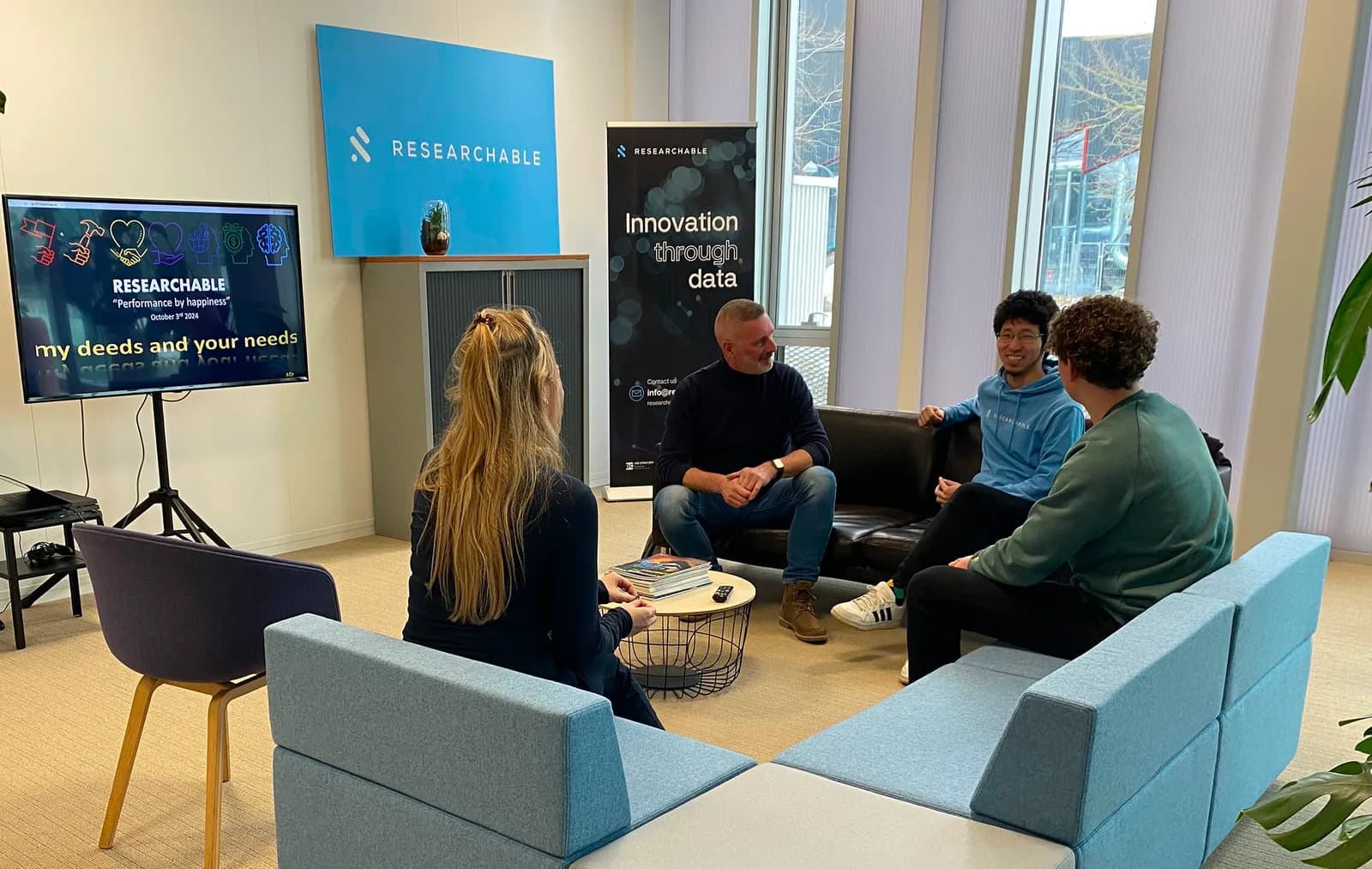 Researchable-collega’s in overleg in de kantoorlounge tijdens een ZIPon-reviewsessie, met een scherm en een Innovation through data-banner